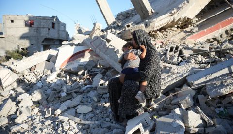 Aaliyah* holds her daughter on the remains of a damaged building in Gaza, October 2024. The mother of six built a temporary shelter opposite her demolished house and depends entirely on aid to feed her family. *Name changed to protect identity