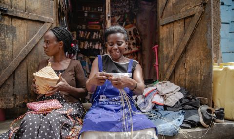 Cossy (pictured right) weaves a basket in front of her shop in Kampala, Uganda
