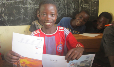 Zephelin, full of smiles, holding cards from his sponsor at school in Burundi