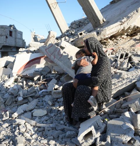 Aaliyah* holds her daughter on the remains of a damaged building in Gaza, October 2024. The mother of six built a temporary shelter opposite her demolished house and depends entirely on aid to feed her family. *Name changed to protect identity